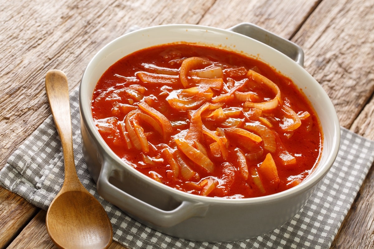 Tocana cu ceapa, usturoi si condimente in sos cebolada, in vas ceramic rotund, alaturi de o lingura de lemn, pe un stergar. Unul dintre cele mai populare sosuri din lume