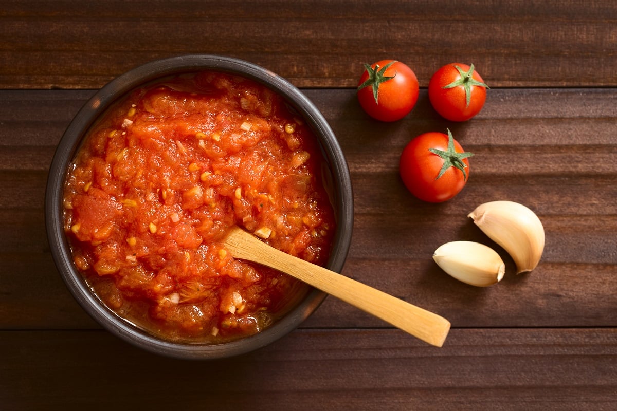 Sos traditional italian marinara, facut in casa, sos de roșii, făcut din roșii, usturoi oregano și sare, servit in bol rustic cu ingredientele asezate in lateral, fotografiat de sus asezat pe lemn inchis la culoare