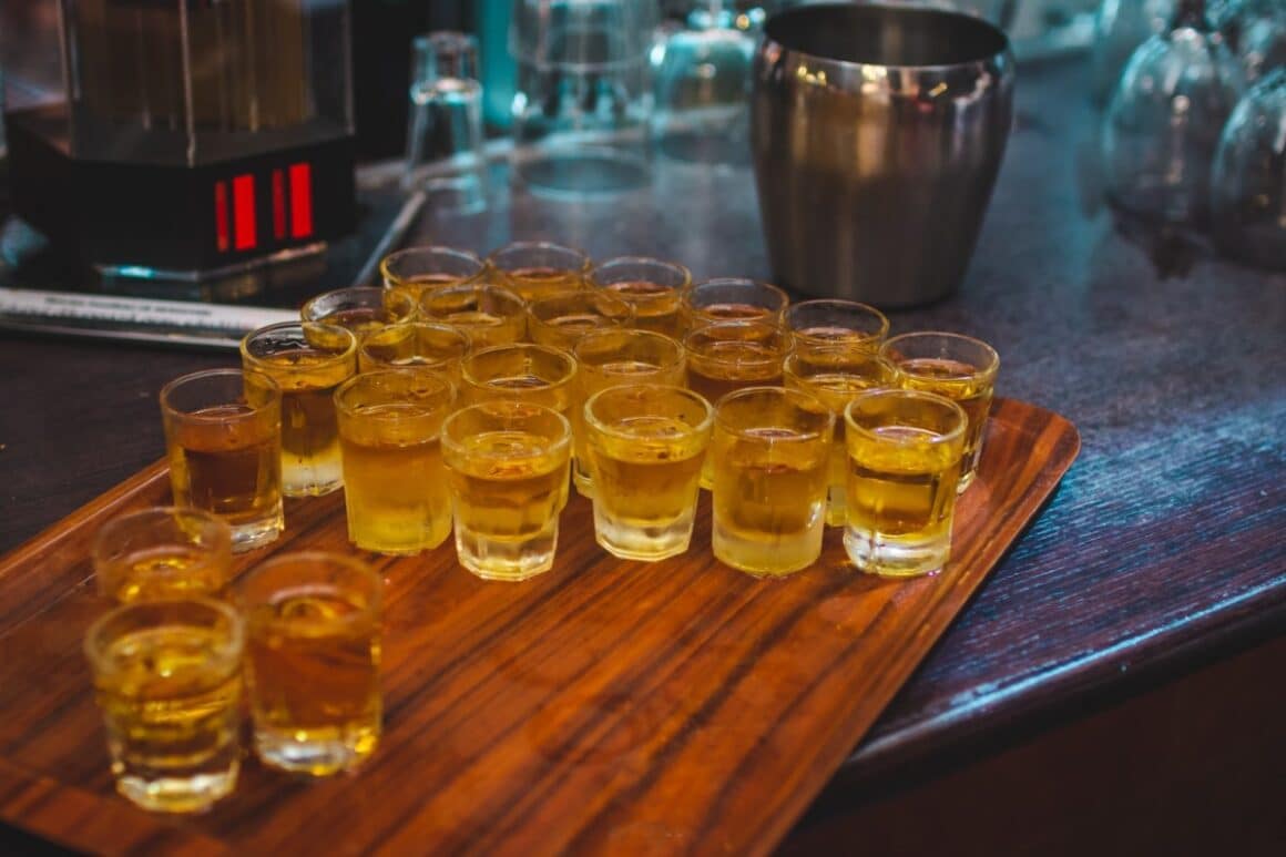 mai multe paharute de țuică înșirate pe un platou de lemn - băuturi românești tradiționale