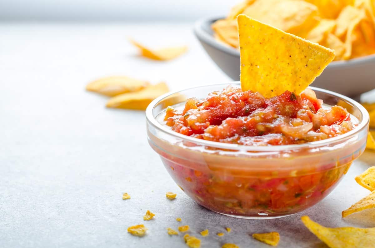 sos salsa tradiționakl mexican, in bol de sticla langa un bol cu tortilla in fundal. close up, cu loc pentru text, imagine orizonatala