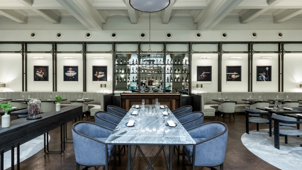 prim plan cu o masa lunga, cu scaune tapitate, bleu, iar in fundal barul de la Blank Restaurant din hotel Marmarosch, unde să ieși cu prietenele în București