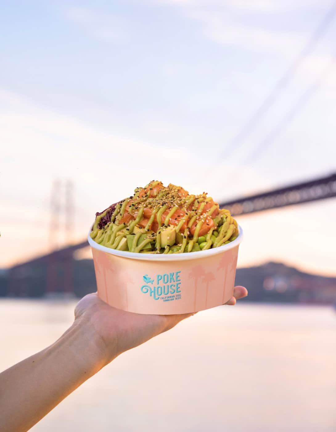 prim plan cu un poke bowl iar in fundal un pod, la apus