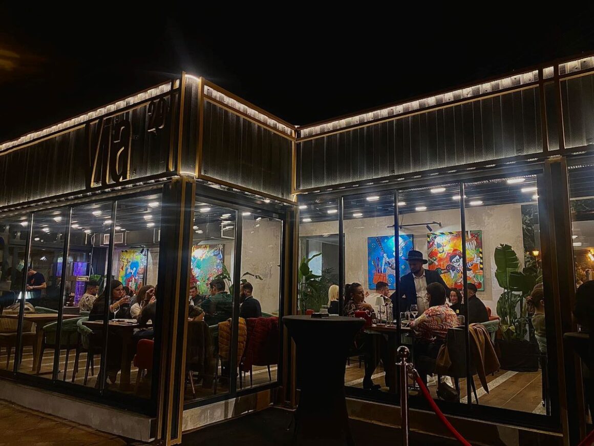 Via29 fotografiat din afara, seara, cu oameni care iau masa inauntru, unul din restaurante Oradea