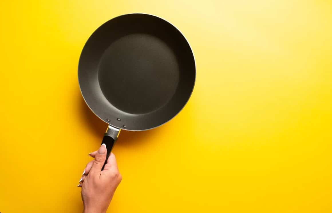 o femeie tine o tigaie din teflon fotografiata pe un fundal galben