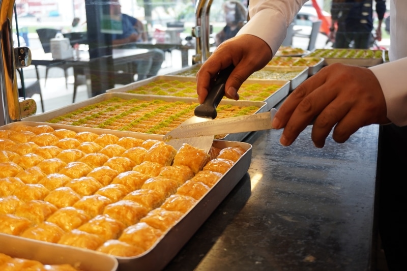 tavi cu baclava din care cineva ia cu o spatula