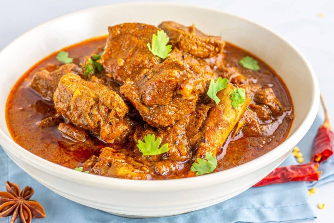 o portie de curry indian este servit alaturi de un ardei iute intr-un bol alb