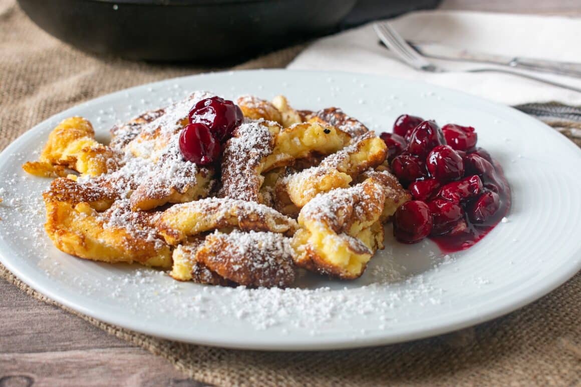 Kaiserschmarrn, clătite austrice, swrvite in farfurie alba pudrate cu zahar si cu vinie alaturi