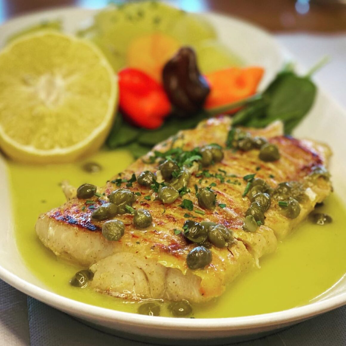 o portie de salau cu sos verde, capere și lamaie din meniul restaurantului laguna verde