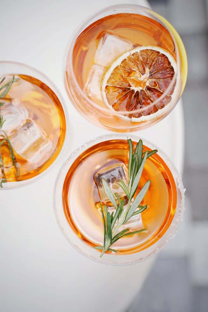 trei pahare de aperol spritz decorate cu o felie de portocala dezhidtratată și o crenguță de rozmarin