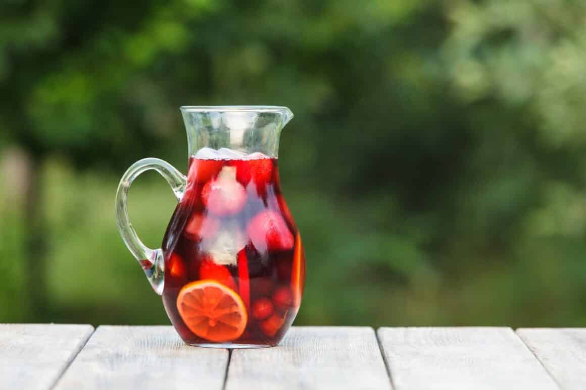 carafa de sangria fotografiata pe o masa iar in fundal verdeata, blurat