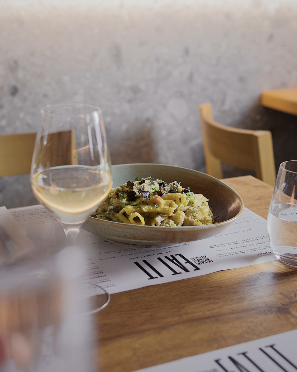 farfurie de paste cu sos alb, pe masa in restaurant alaturi de 1 pahar de vin alb, la Eat IT restaurante Oradea