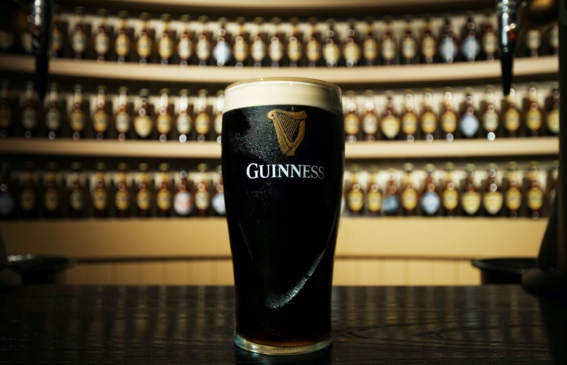 Un pint de guinness fotografiat pe tejgheaua unui bar de beri cu multe sticle in fundal - imagine concept despre berea Guiness