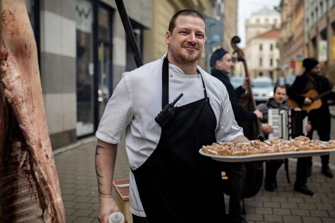 unul dintre bucatarii restaurantului lokal din praga tine in mana un platou cu aperitive pe terasa restaurantului