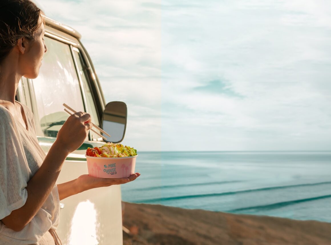 femeie sprijinita de o masina mananca dintr-un poke bowl iar in fundal se vede marea