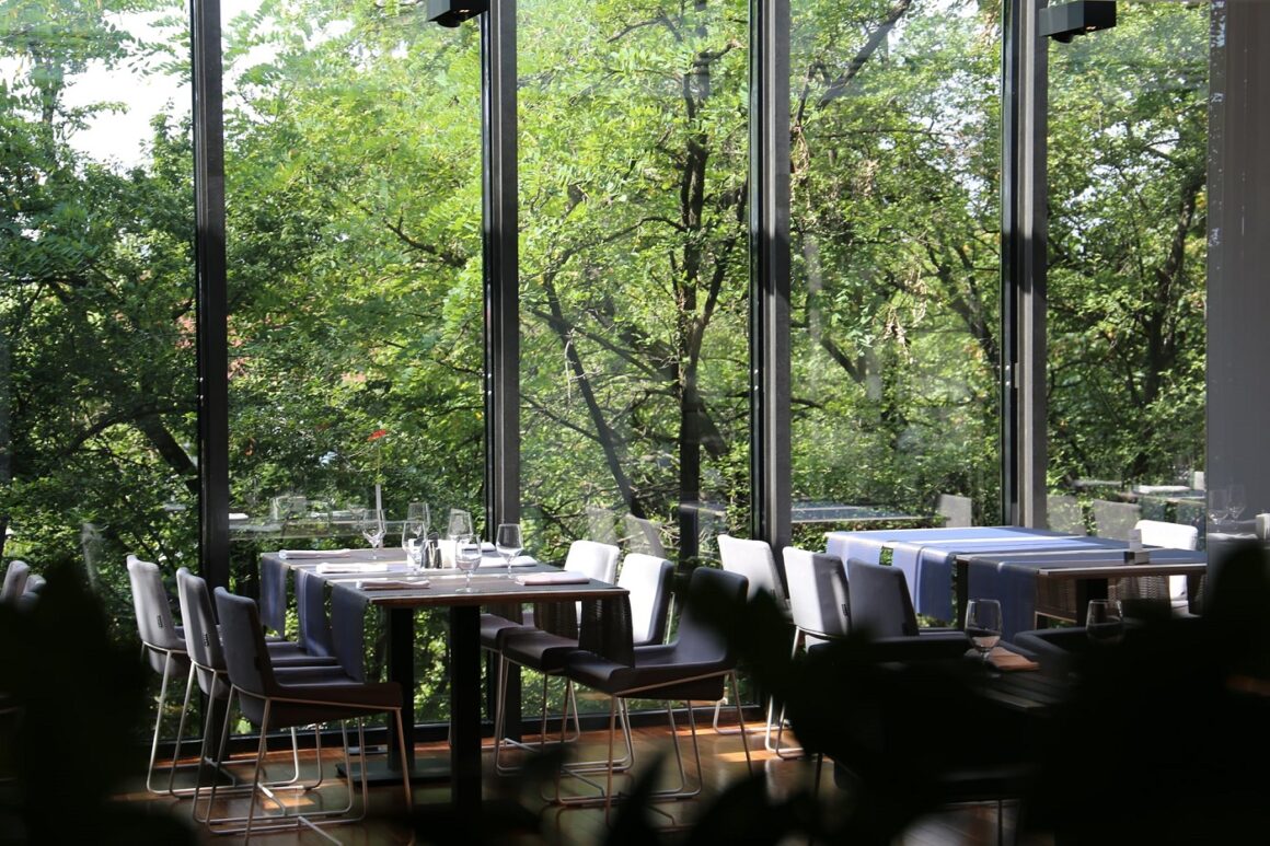 Mese asezate in fata unor ferestre mari prin care se vad copacii inverziti la restaurant Privo din Targu Mures - unul din restaurante destinatie din țară