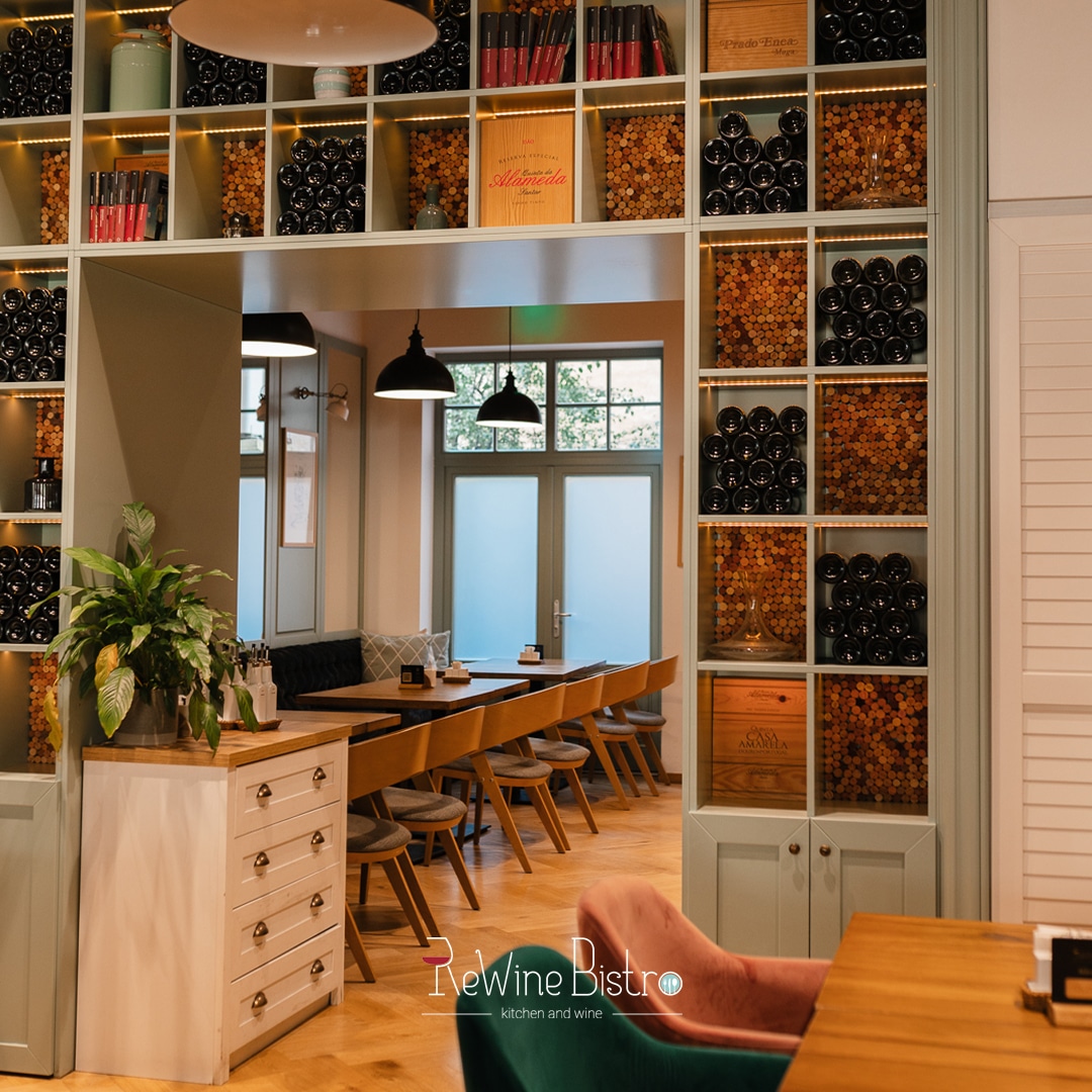 imagine din Rewine Bistro din Oradea, cu mese fotografiate preintr-un cadru de usa inramat cu rafturi cu sticle de vin