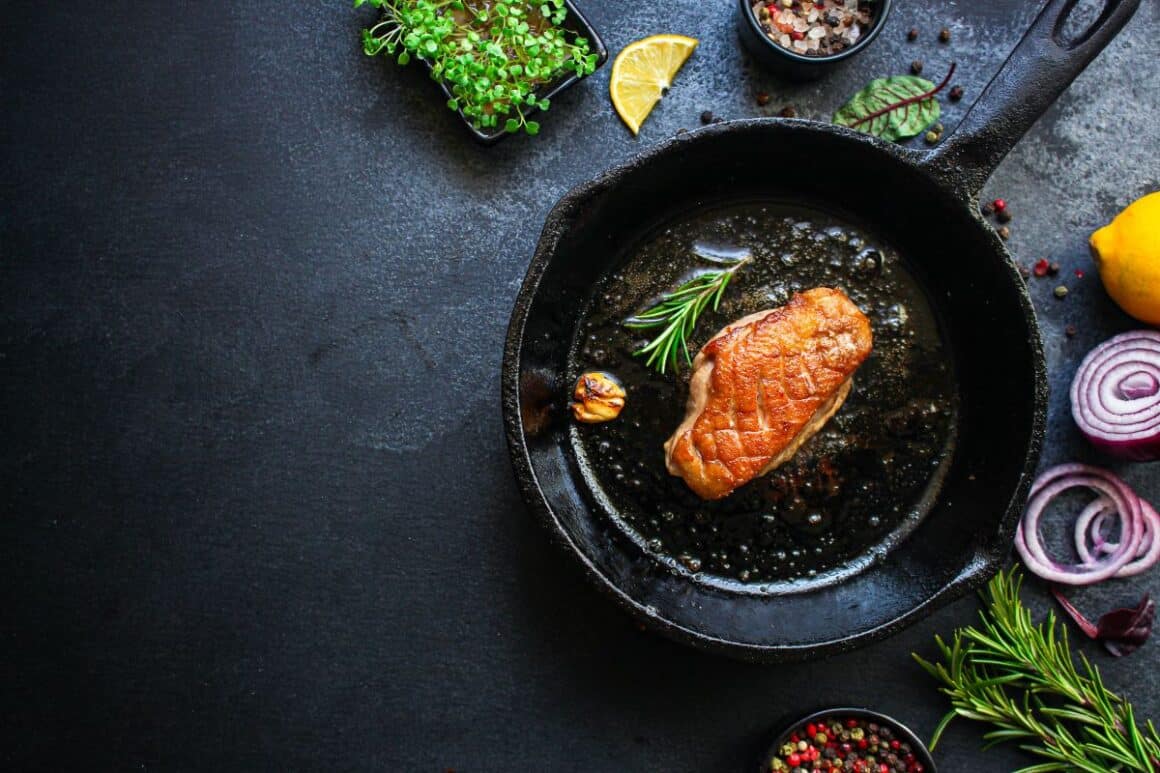 un piept de rața gatit intr-o tigaie de fonta, alaturi de verdeturi și condimente - tipuri de tigăi