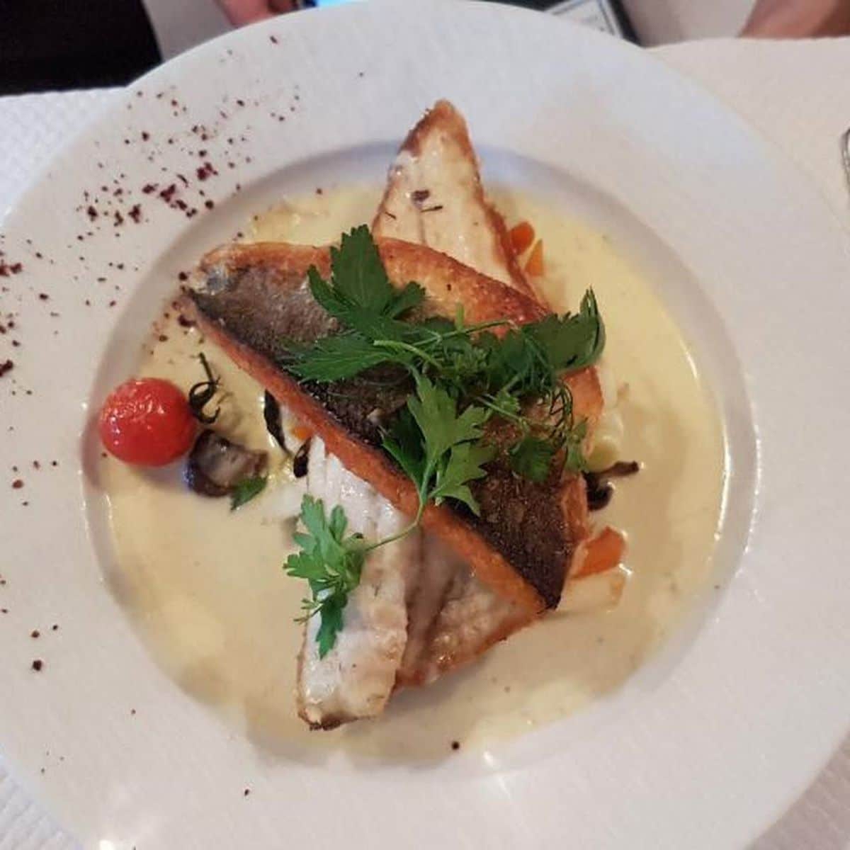 O PORTIE DE PEȘTE PANE CU SOS ALB INTR-O FARFURIE ALBA