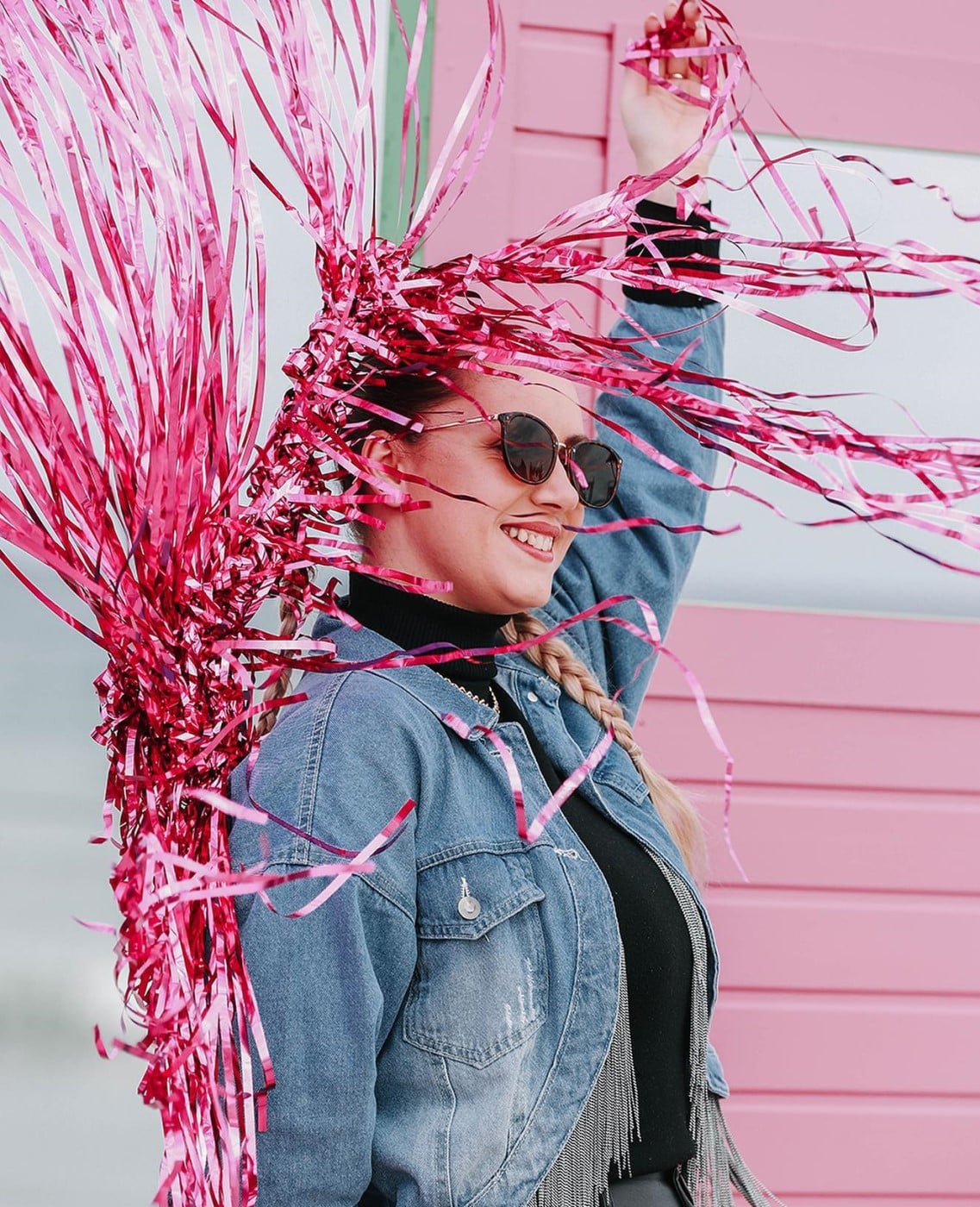 fata in geaca de blugi, cu ochelari, pozeaza in fata unui perete roz