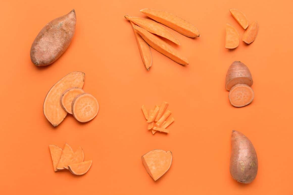 Carofi dulci intregi, taiati pe jumatate si felii, fotografiati pe fundal portocaliu