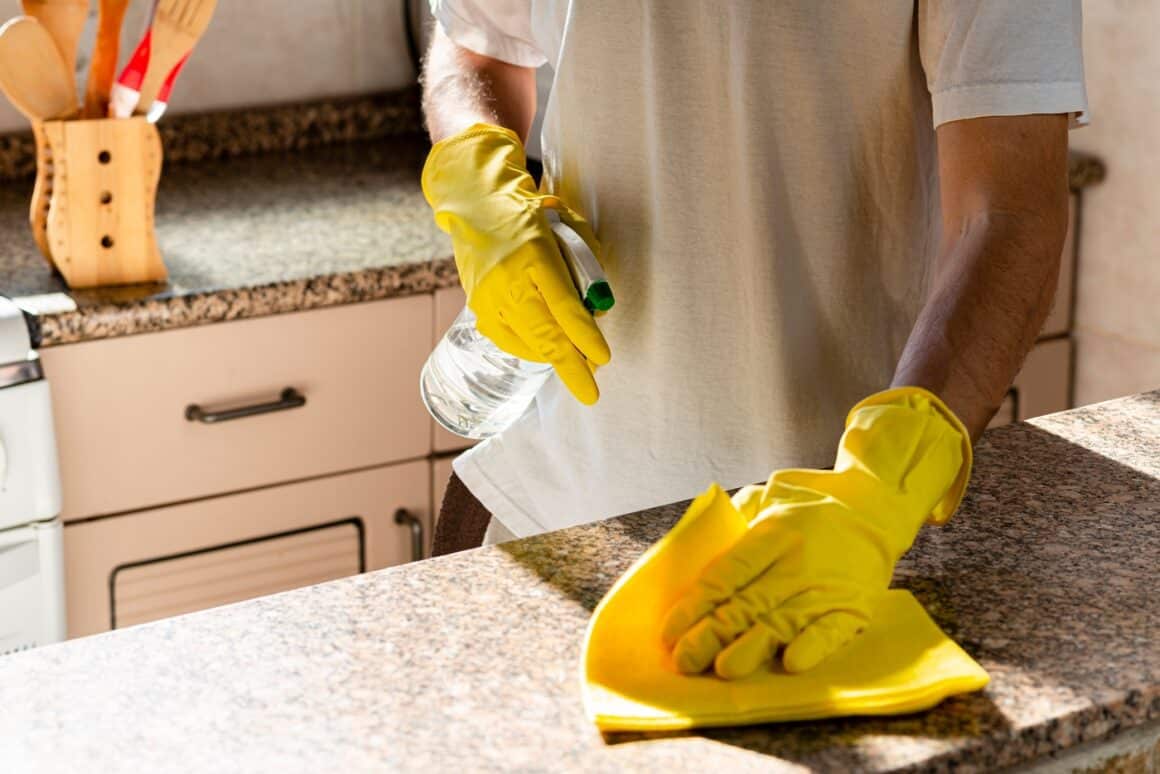 barbat care spala baltul de marmura in bucatarie, folosind produse naturale de curățenie și manusi galbene