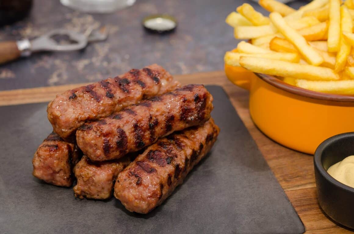 mici pe un platou negru, alaturi de o oala cu cartofi prajiti