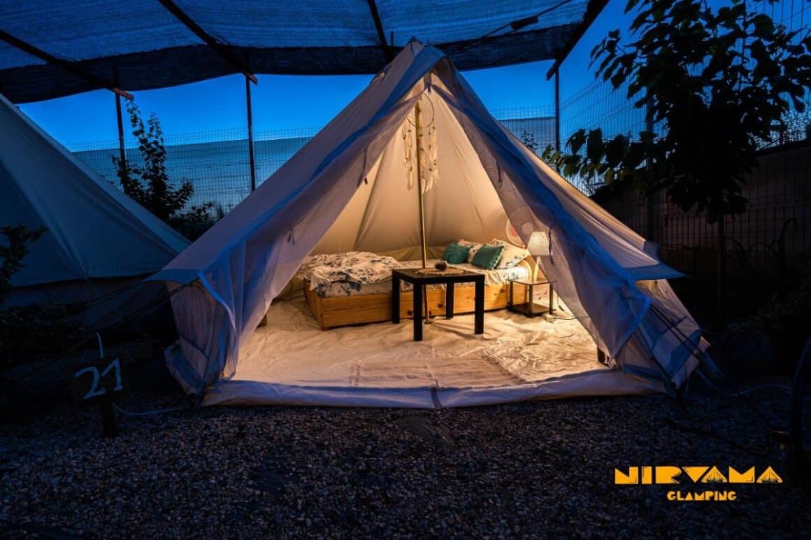 cort de glamping fotografiat seara, iluminat, mobilat cu pat, la Nirvama Glamping tent