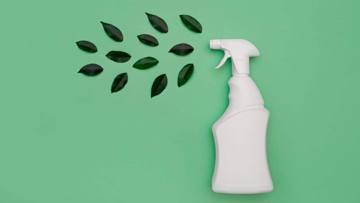 spray de curatenie alb, pe fundal verde, alaturi de frunzulite verzi - imagine concept pentru produse naturale de curățenie