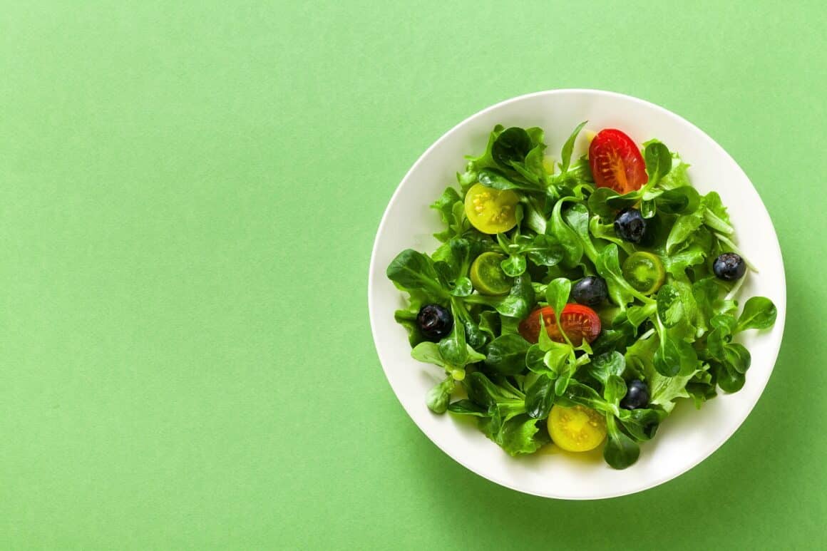 farfurie cu salata proaspata, cu rosii si masline, fotografiata de sus pe fundal verde