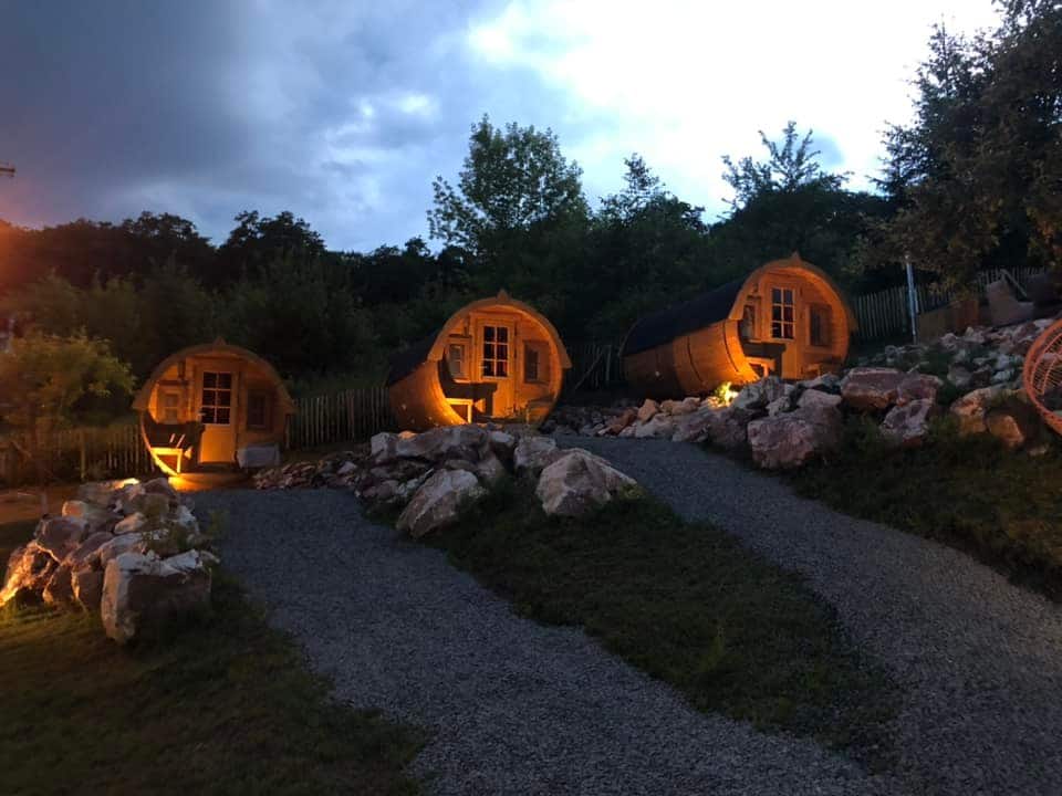 3 spatii de cazare sub forma de butoaie, fotografiate sera, cu lumini aprinse, la Complexul Butoaiele Transilvaniei