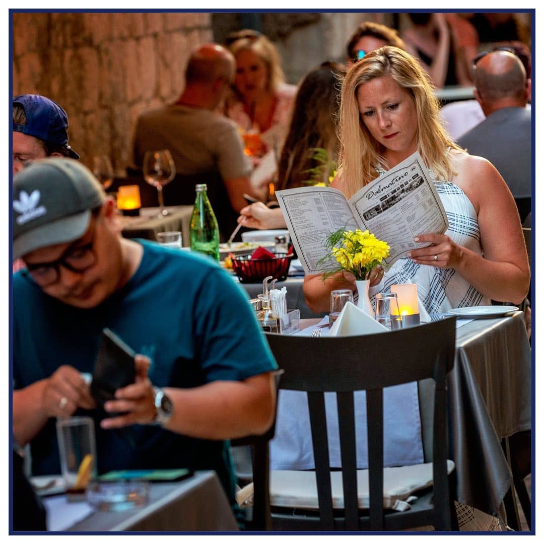 o femeie cinteste ziarul sau meniul la o masă a unei terase
