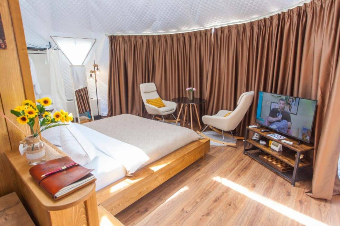 interiorul unui cort de glamping de lux, cu pat masiv, fotolii si televizor la Glamont, Farcașa, Valea Bistriței.