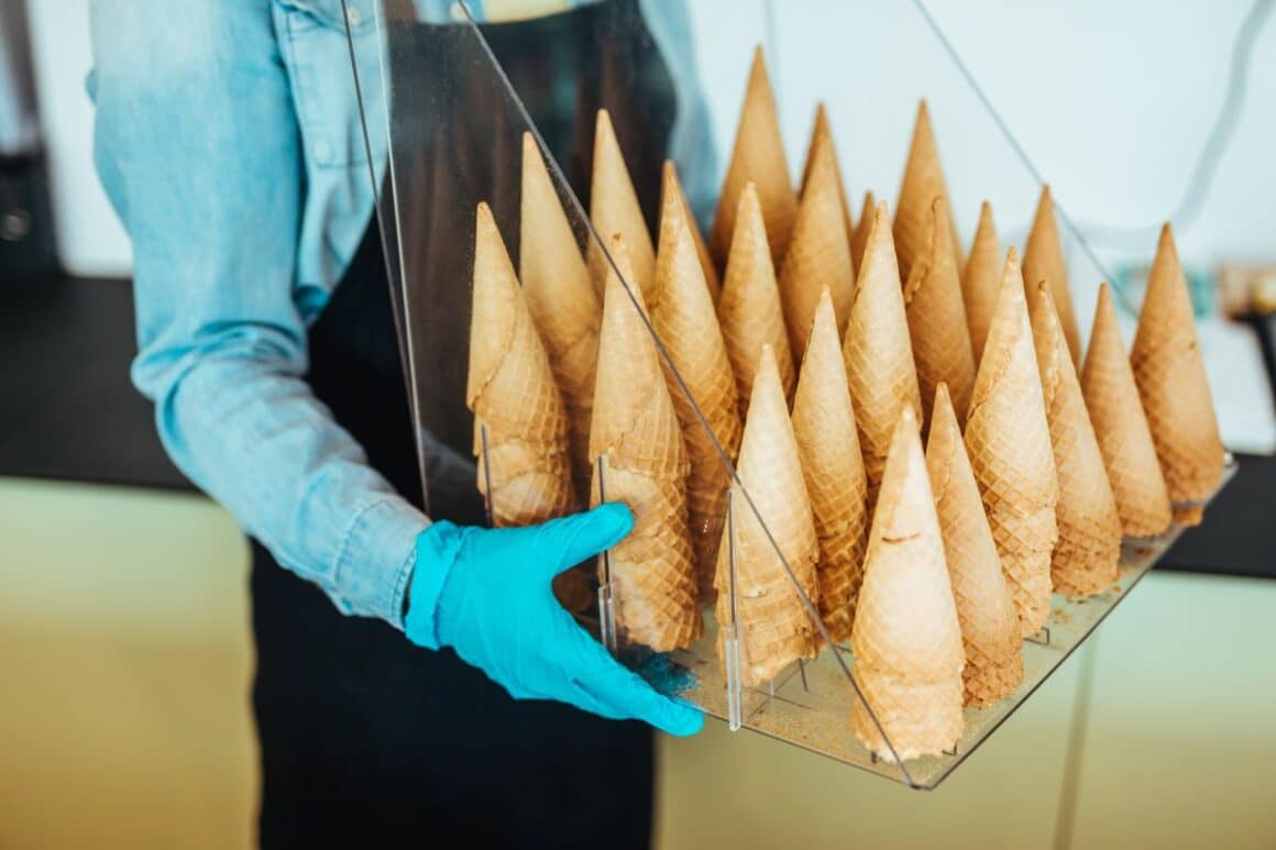 un gelatier tine in maini un suport din plexiglass incarcat cu cornete pentru inghetata