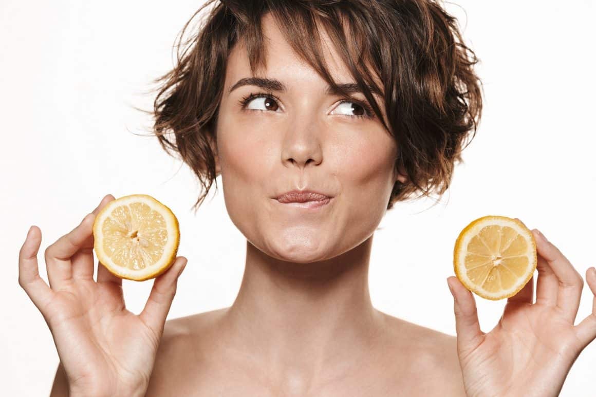 Portretul unei femei tinere, bruneta, care tine in maini cate o jumatate de lamaie si zambeste. FUndal izolat. Alimente pentru piele frumoasă și sănătoasă