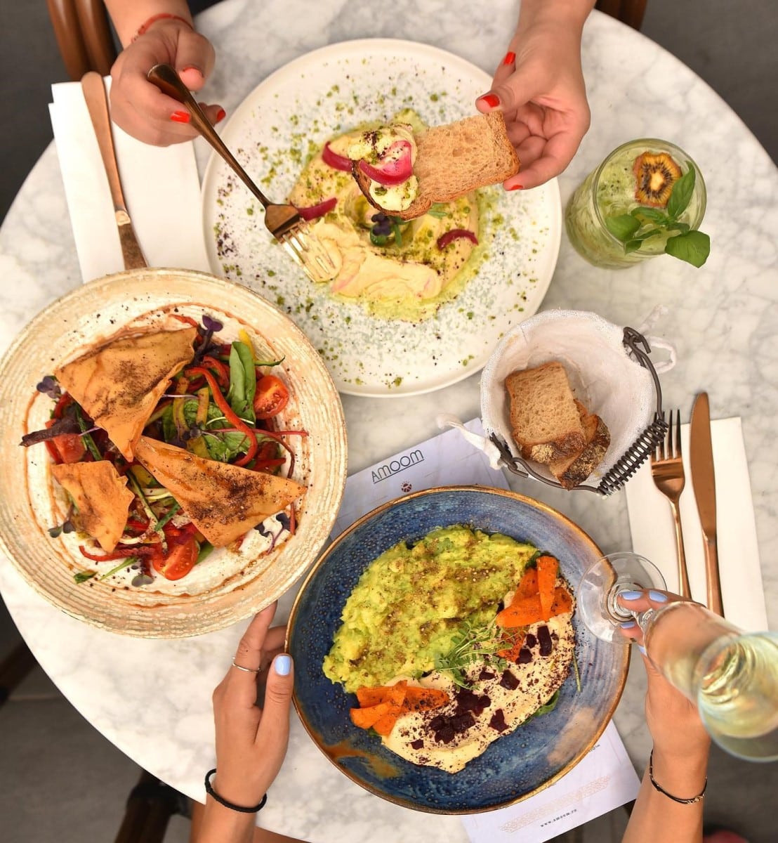 masa fotografiata de sus, din care 2 cu hummus, din care mananca 2 femei