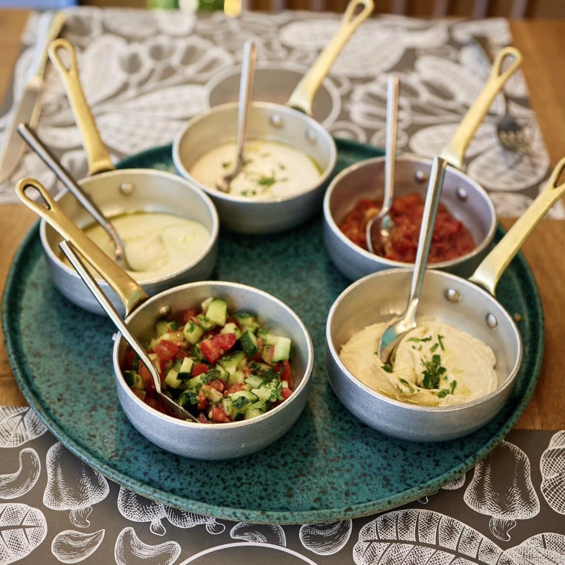 platou mare albastru, cu gustari arabesti puse in craticioare mici metalice, dintre care unul cu hummues, de la Caju by Joseph Hadad