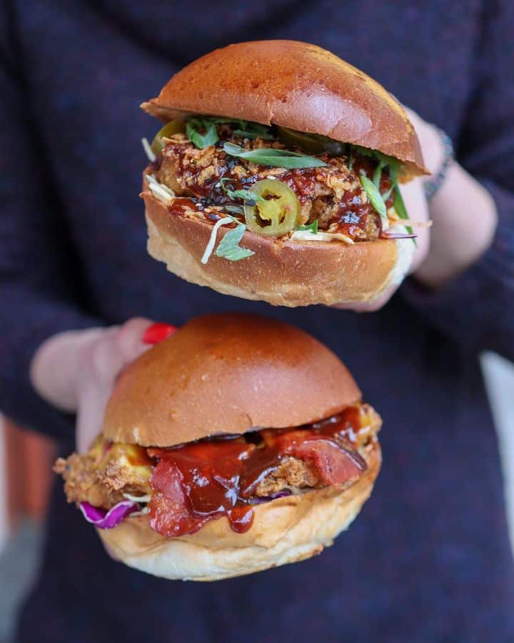 Femeie care tina in mana doi burgeri fotografiati de aproape, unul din ele Korean burger de la Le Bab Fried Chicken.