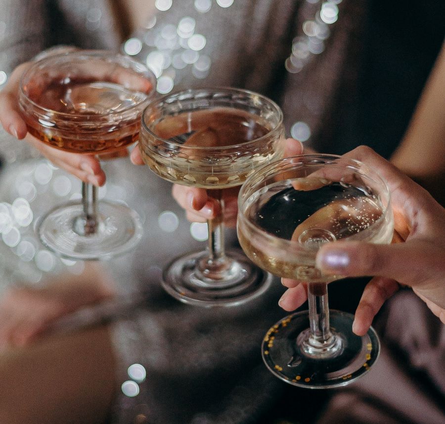 trei tinere frumoase dau noroc cu cate un pahar de cocktail, una dintre ele avand o rochie aurie cu paiete. Imagine pentru forma paharului de cocktail clasic