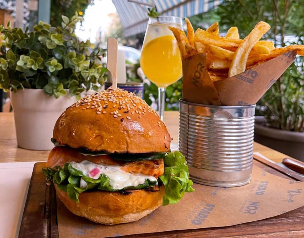 Burger cu somon si sos remoulade langa o cutie din tabla cu cartofi prajiti de la Stadio.