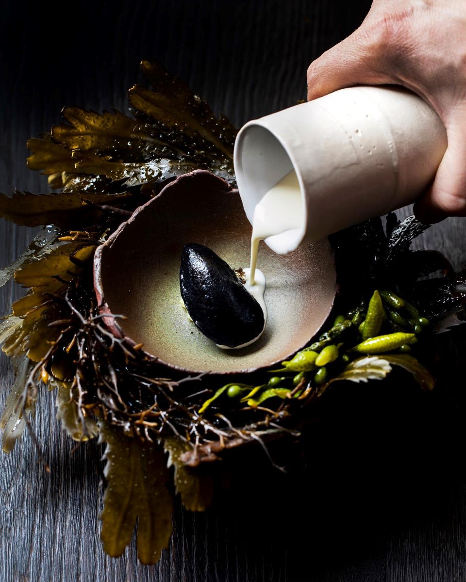 o mână de bărbat toarnă un sos alb peste o scoica neagră