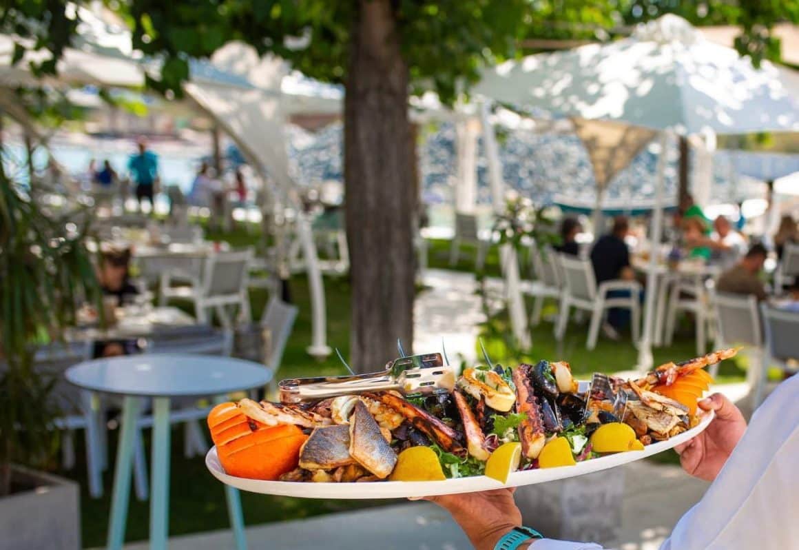prim plan cu un platou cu fructe de mare, iar in fundal terasa pe gazon si marea, blurate. Cherhanale de pe litoralul românesc