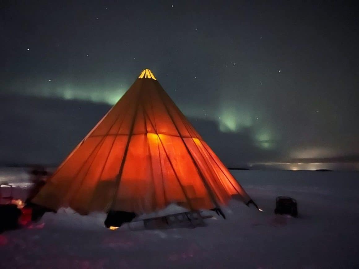 o lumina deveghe trece prin panza unei iurte iar în spate se văd luminile nordului. Cină extravagantă 