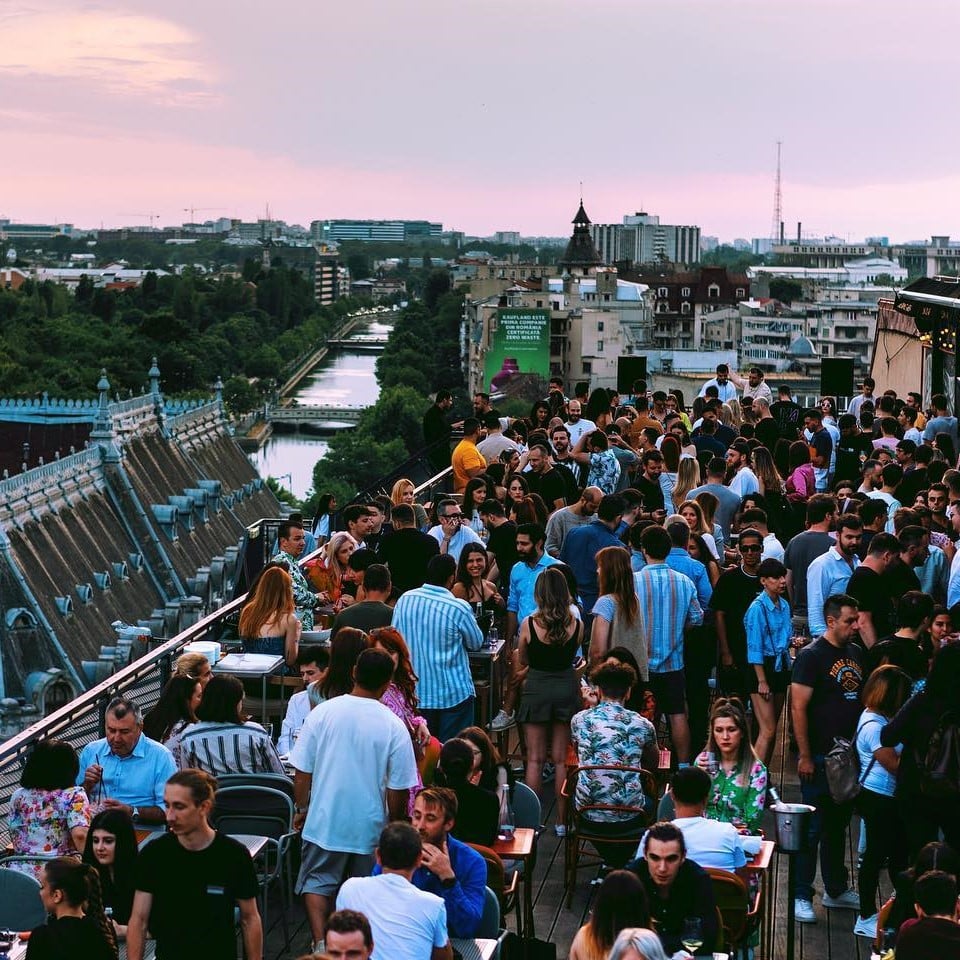 Terasa rooftop Linea din Bucuresti, plina de oameni car erad si se distreaza, iar in fundal Bucurestiul vazut de sus