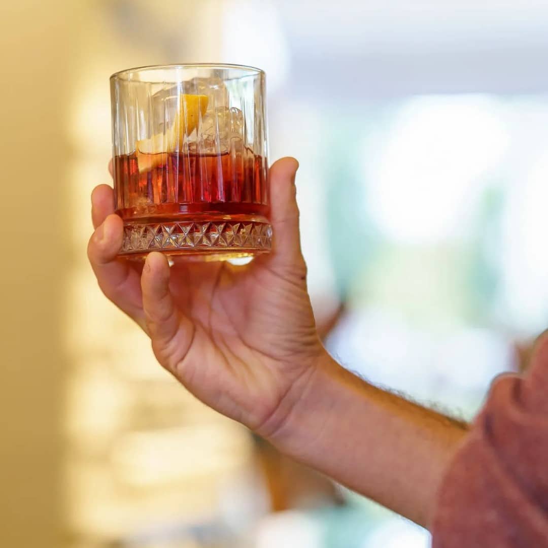 closeup cu o persoana care tine in mana un pahar de negroni. Cocktail la terasă în București