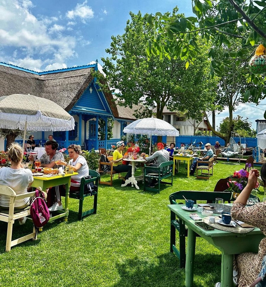 oaemni asezati la mai multe mese colorate iau masa in curtea de la Casa Ilinca din Deltă