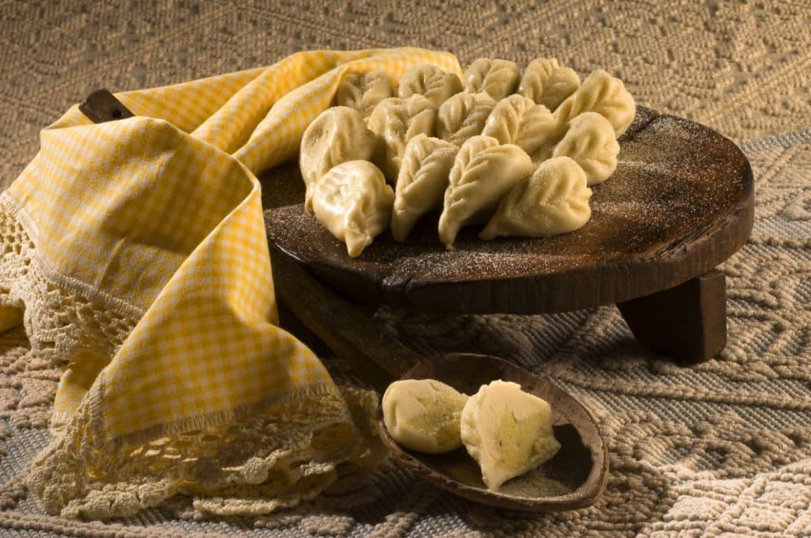 Culurgiones, niște raviolli mai grase, sunt asezate pe un suport rotund de lemn, alături de un stergar tradințional. Preparate tradiționale din Sardinia