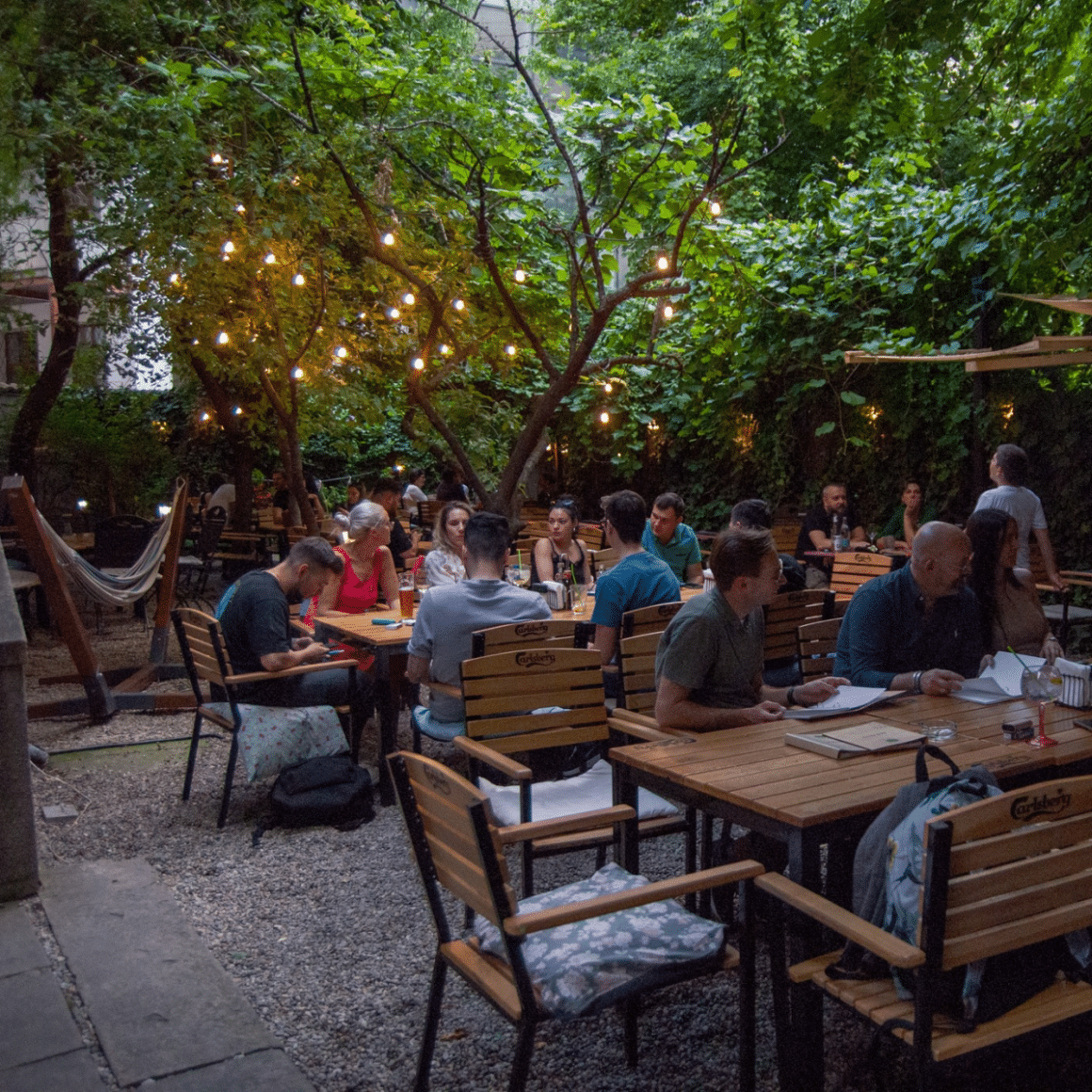 Gradina de la Lente Bucuresti, cu mese de lemn, multi copaci si luminite decorative