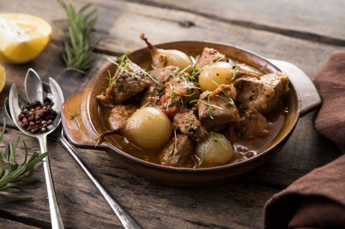 Pecora in cappotto, o mancare tipic sardă, este servita intr-un bol traditional, pe o masă de lemn, alături de condimente