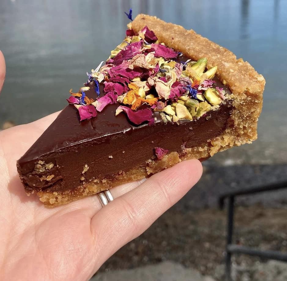 felie dintr-o tarta cu ciocolata raw vegana, decorata cu petale uscate de flori