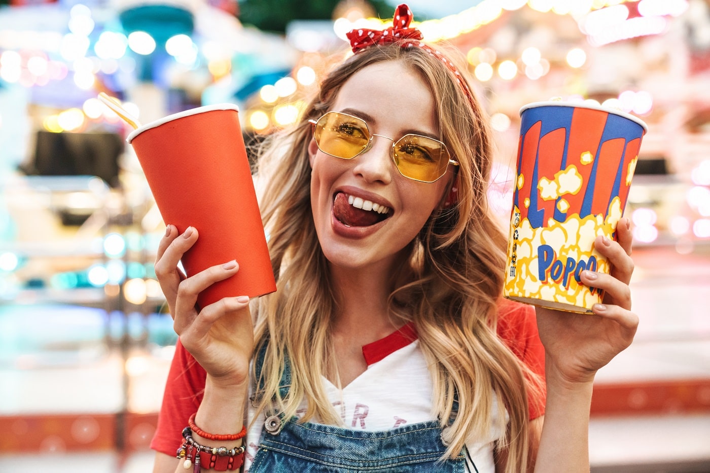 Fata tanara, cu ochelari, zambeste strengareste si tine in mana o galeata cu popcorn si un pahar de plastic cu suc. Despre popcorn